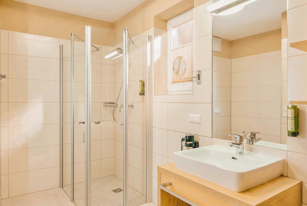 Modernes Badezimmer mit begehbarer Dusche, hellem Fliesenboden und Holzwaschtisch.