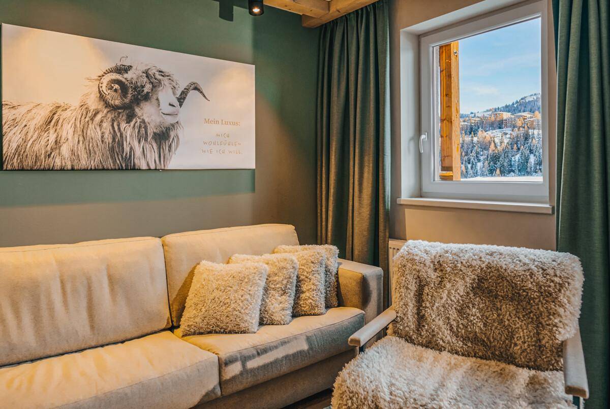 Gemütliches Wohnzimmer im alpinen Stil mit beiger Couch und Fensterblick auf die Winterlandschaft.
