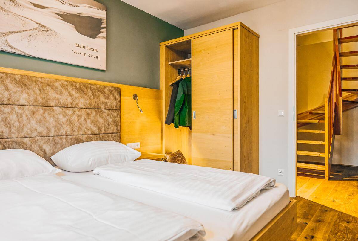 Schlafzimmer mit Holzschrank und Zugang zu einer Treppe, im alpinen Stil eingerichtet.