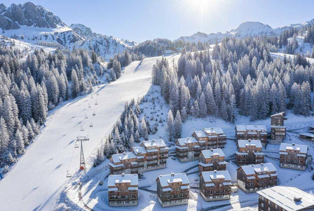 Winterliche Luftaufnahme eines Bergresorts mit verschneiten Chalets und Skipiste.