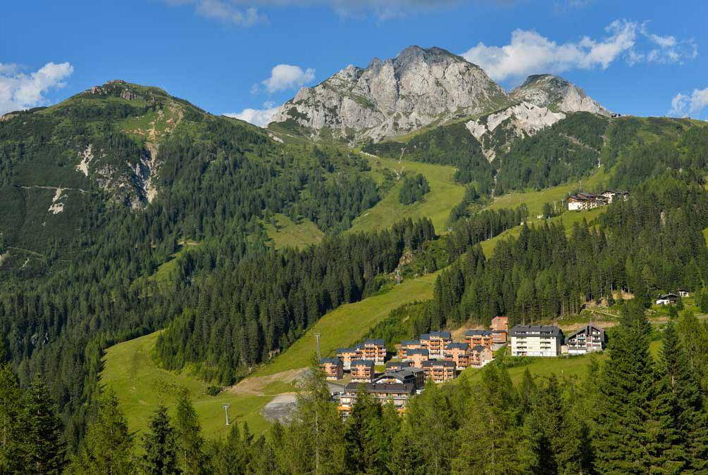 Weitläufiger Blick auf ein Bergresort mit Chalets und grünen Hängen unter einem imposanten Gipfel.