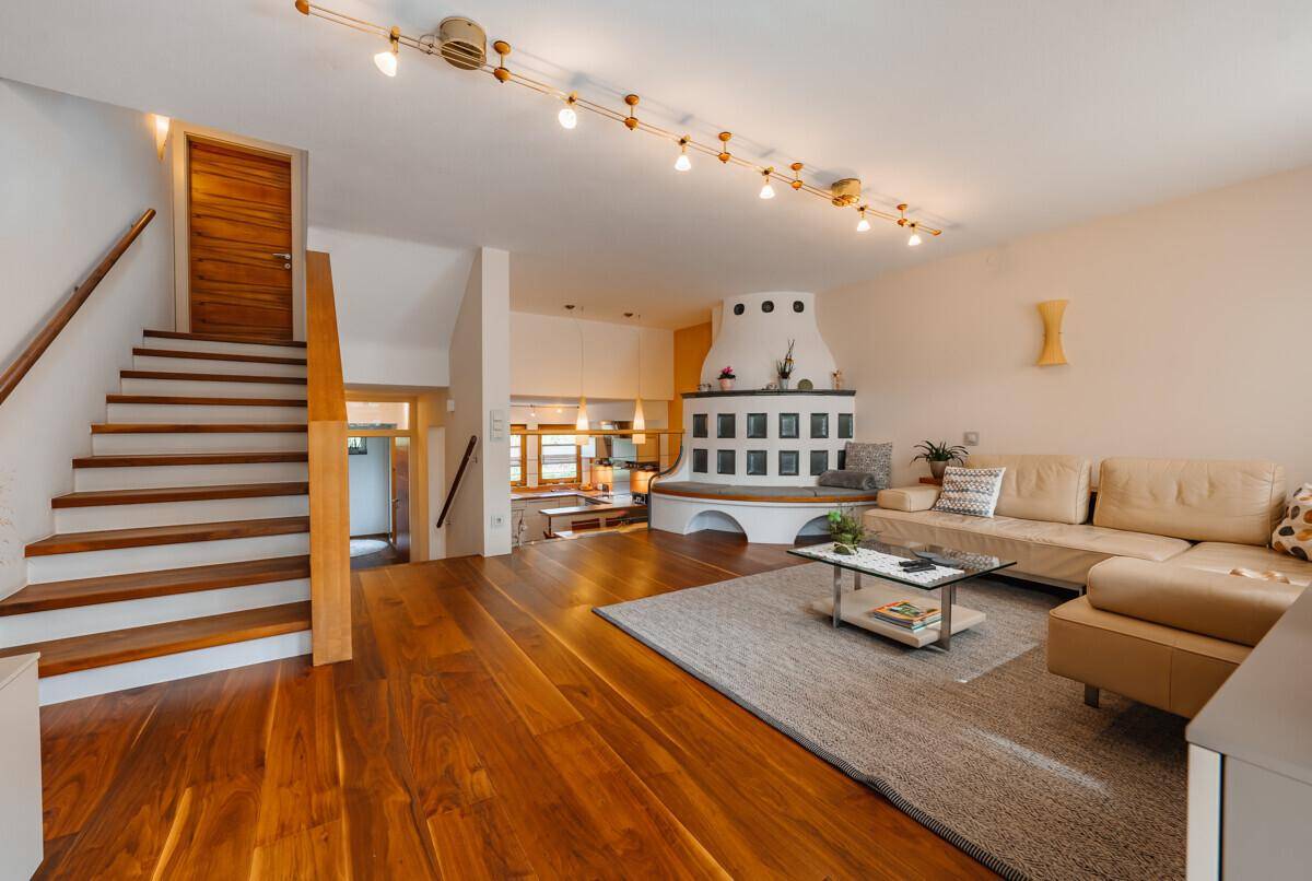 Geräumiges Wohnzimmer mit Holzboden, Kachelofen und Treppe zum Obergeschoss.
