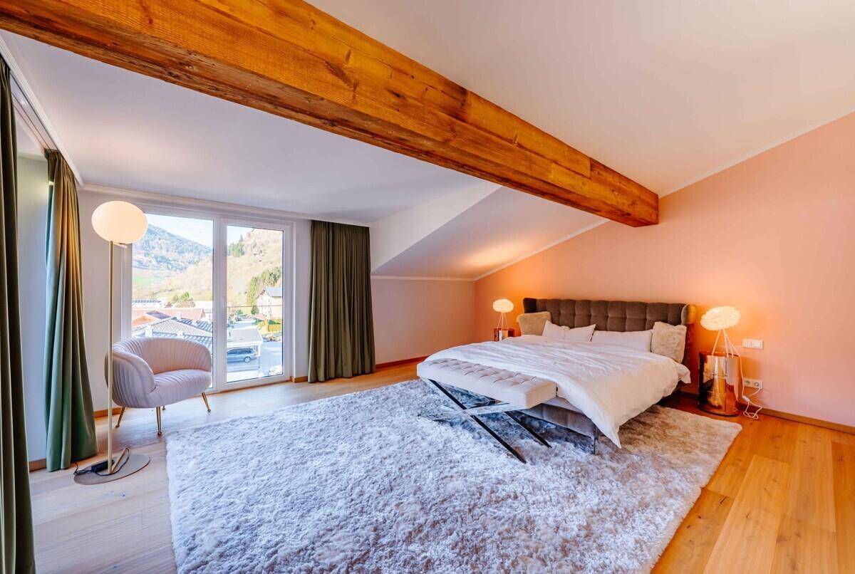 Gemütliches Schlafzimmer mit Holzbalken, Teppich und Zugang zum Balkon.