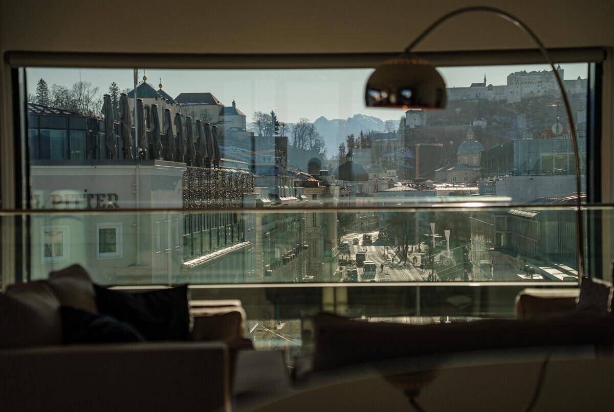 Helles Wohnzimmer mit großem Fenster und Panoramablick auf die Stadt und Berge am Tag.
