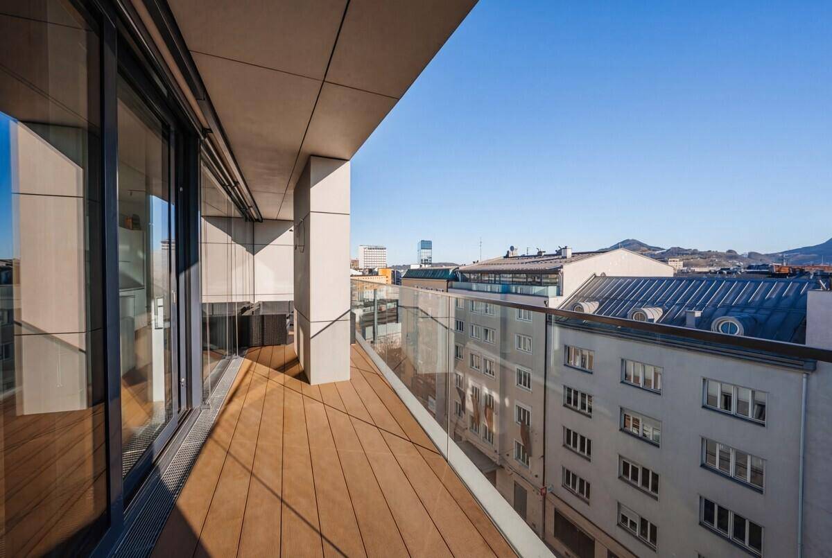 Geräumiger Balkon mit Holzboden und Glasgeländer, bietet weiten Blick über die Stadt.