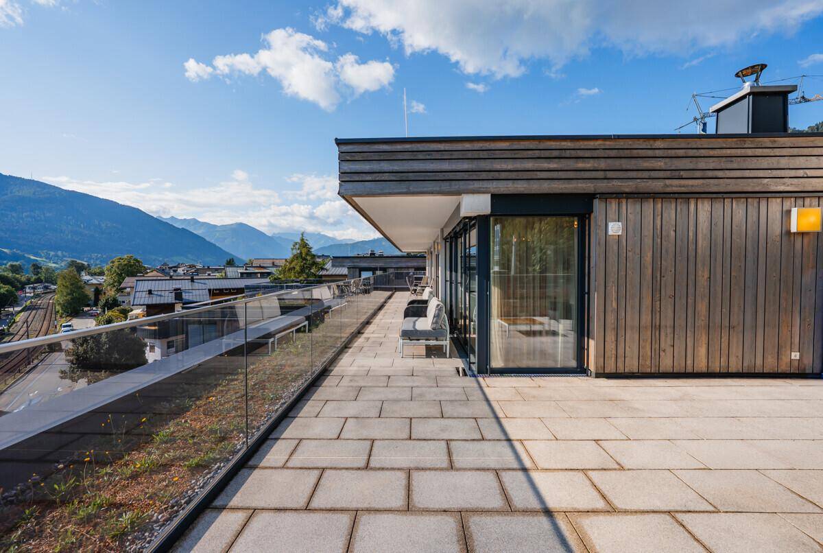 Ausgedehnte Dachterrasse mit Holzfassade und Fliesenboden, umgeben von einer beeindruckenden Bergkulisse.