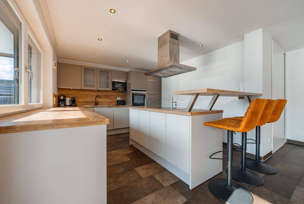 Moderne Küche mit grauen Schränken, Holz-Arbeitsplatten und einer Kücheninsel mit integrierter Bar.