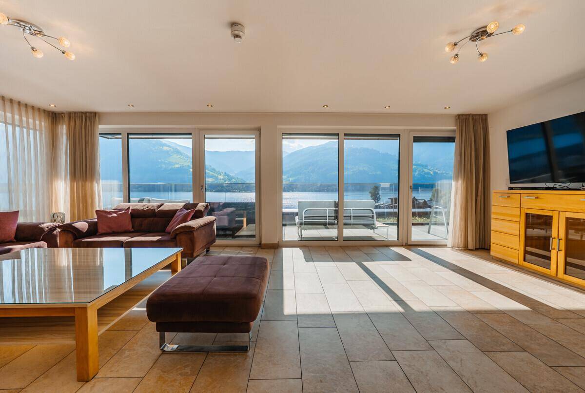 Helles Wohnzimmer mit Zugang zur Terrasse und Panoramablick auf den See und die Berglandschaft.