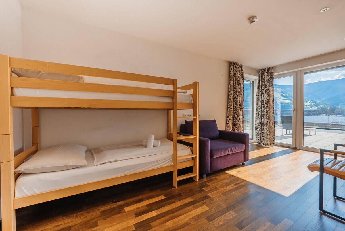Kinderzimmer mit Etagenbett und gemütlichem Sessel, mit Zugang zu einer Terrasse und Bergblick.