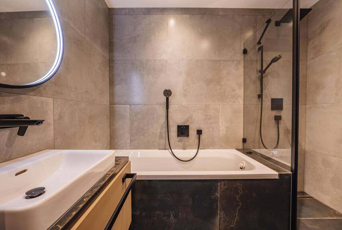 Modernes Badezimmer mit großer Badewanne, Duschbereich und eleganten grauen Fliesen.