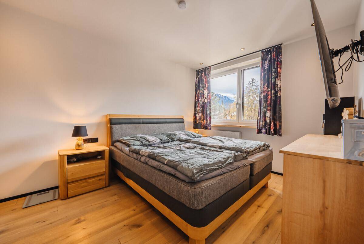 Gemütliches Schlafzimmer mit Holzboden, Doppelbett und Blick auf die Berge.