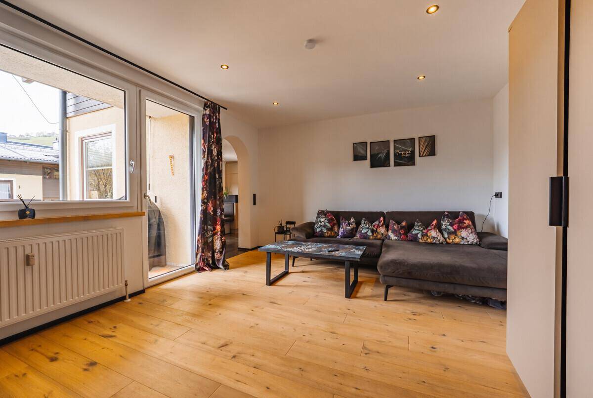 Helles Wohnzimmer mit Holzboden, bequemer Couch und Zugang zu einem Außenbereich.