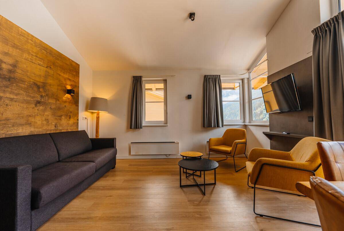 Gemütliches Wohnzimmer mit Sofa, Sesseln und einer Holzwand, bietet eine warme Atmosphäre.