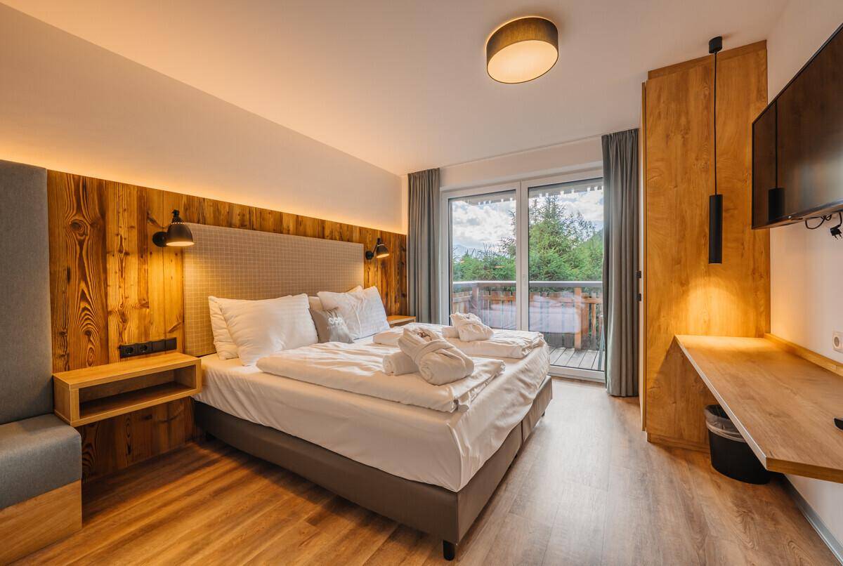 Gemütliches Schlafzimmer mit Doppelbett, Holzelementen und Zugang zu einem Balkon.