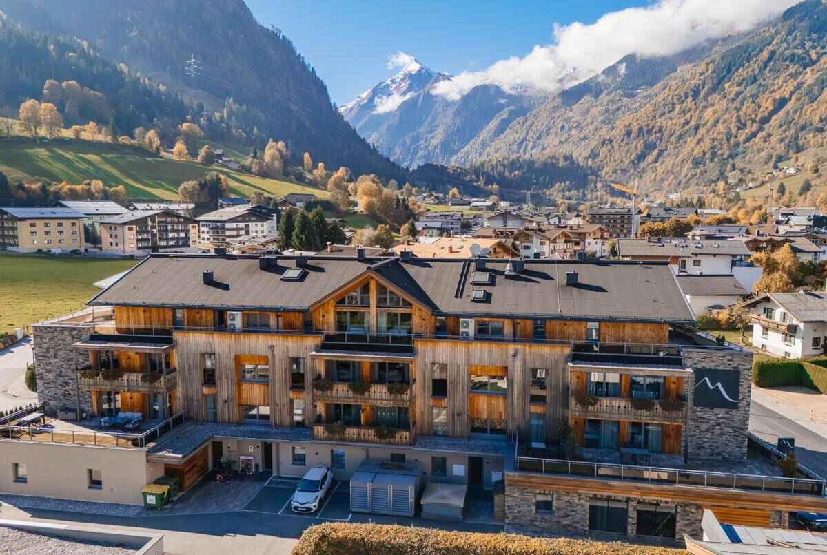 Neubau im alpinen Stil mit Holzfassade und Balkonen, umgeben von einer beeindruckenden Berglandschaft.