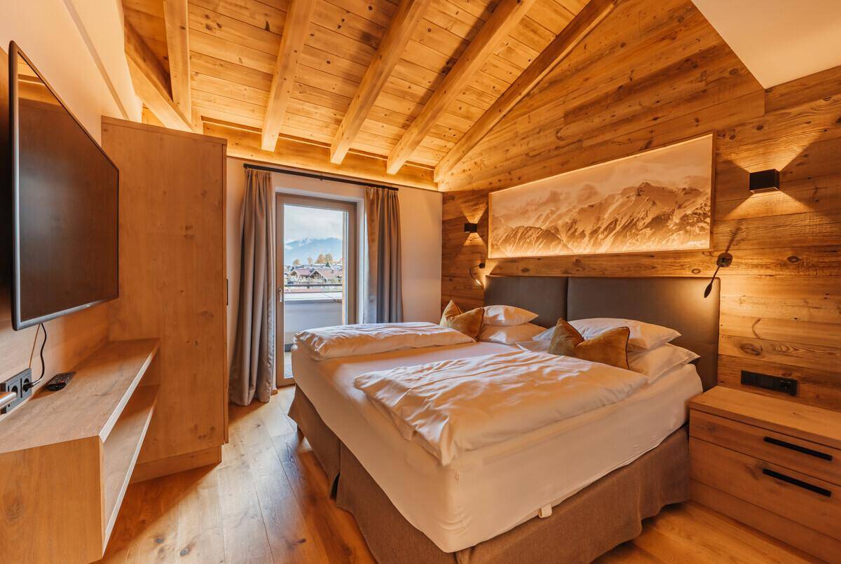 Gemütliches Schlafzimmer mit Holzbalkendecke, Doppelbett und Zugang zu einem Balkon.