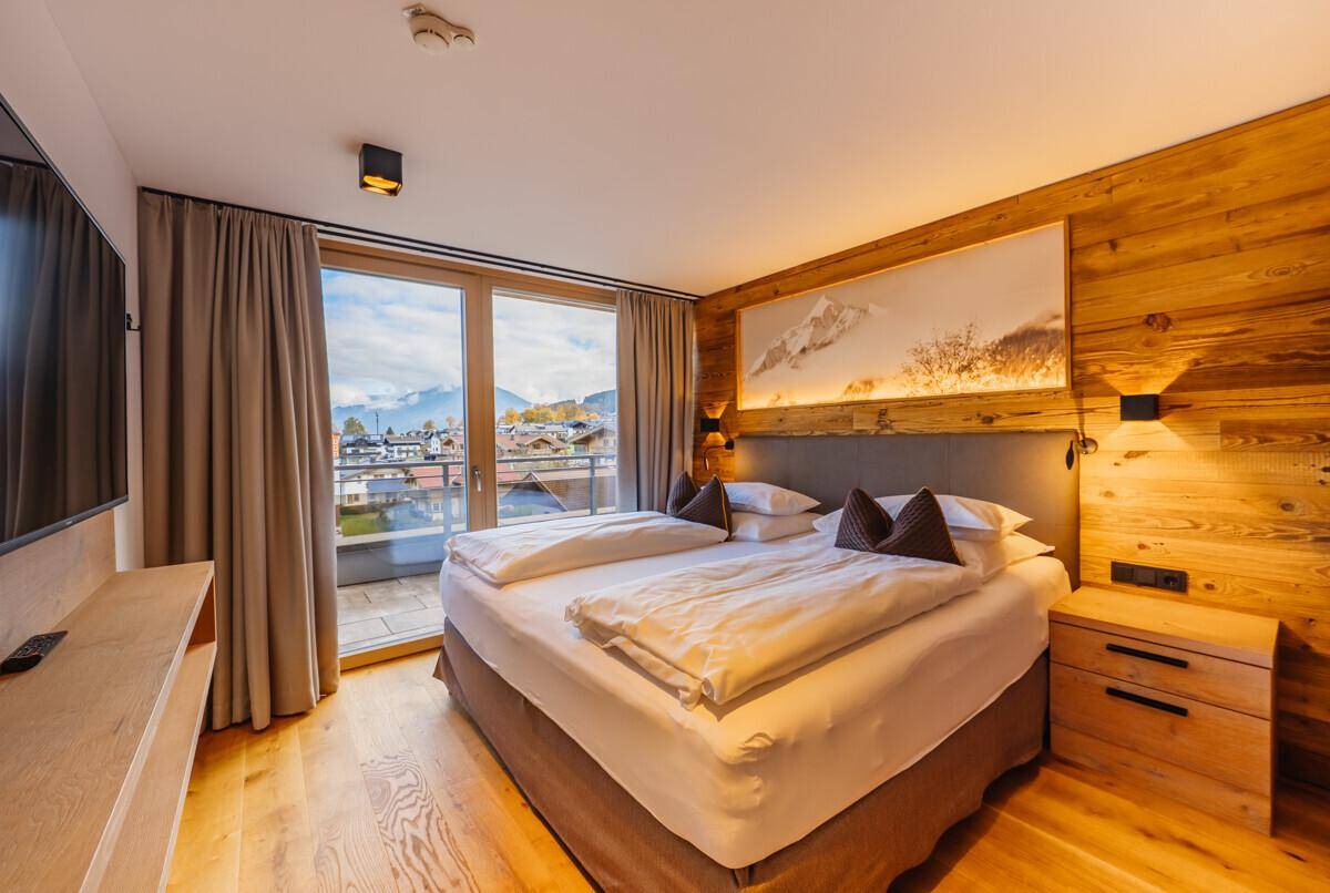 Helles Schlafzimmer mit Holzwänden, Doppelbett und großen Fenstern mit Bergblick.