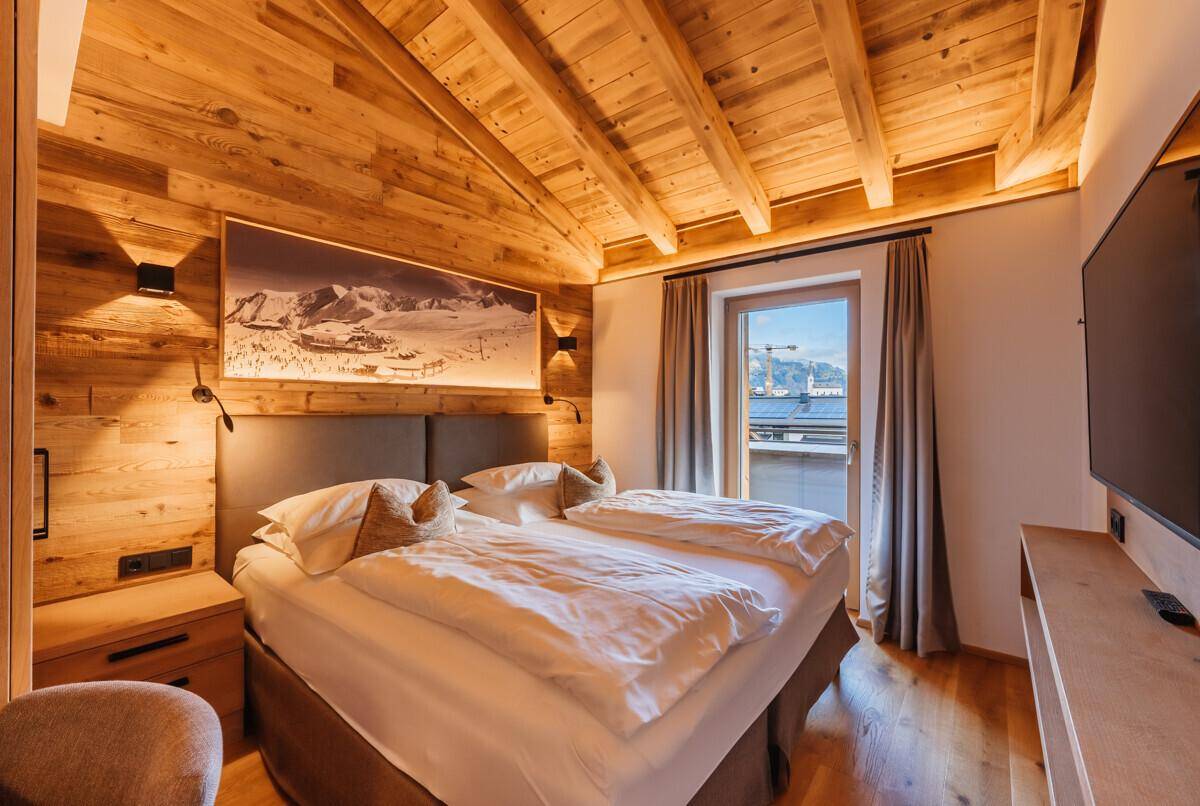 Gemütliches Schlafzimmer im alpinen Stil mit Holzwänden, Doppelbett und Balkonzugang.