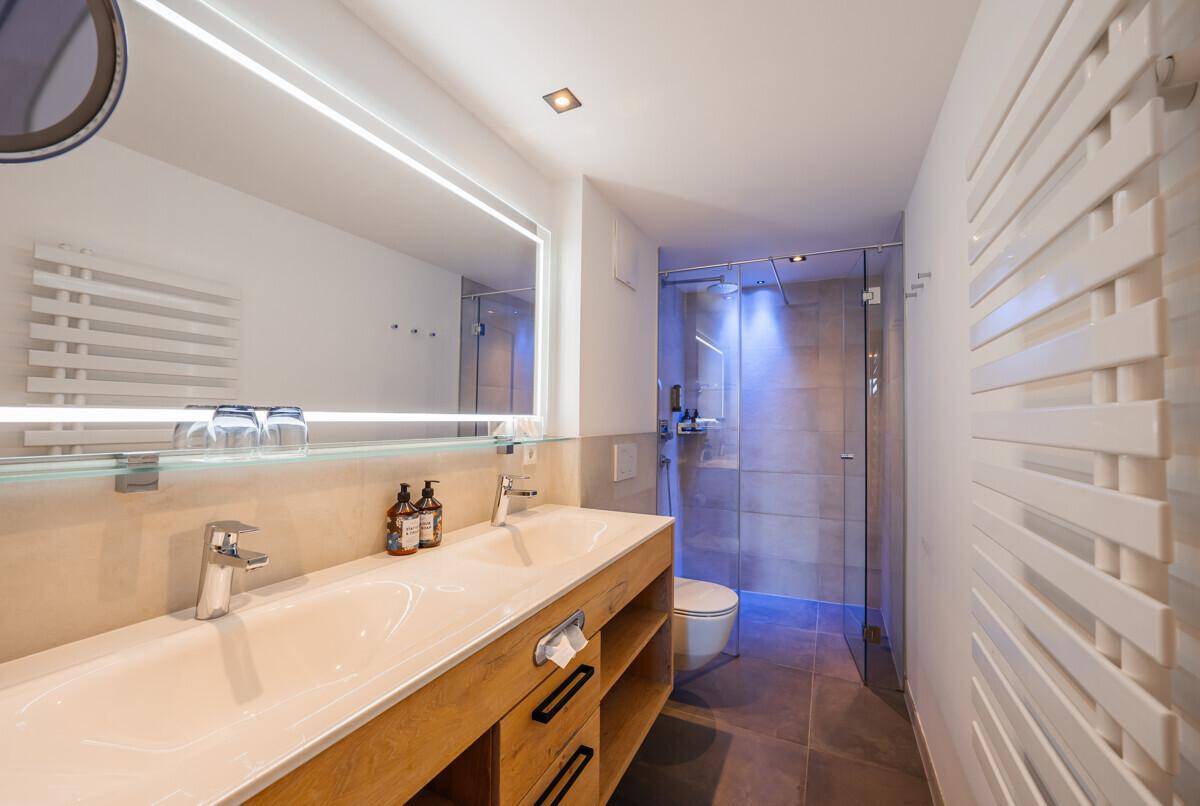 Modernes Badezimmer mit Doppelwaschbecken, beleuchtetem Spiegel und begehbarer Dusche.