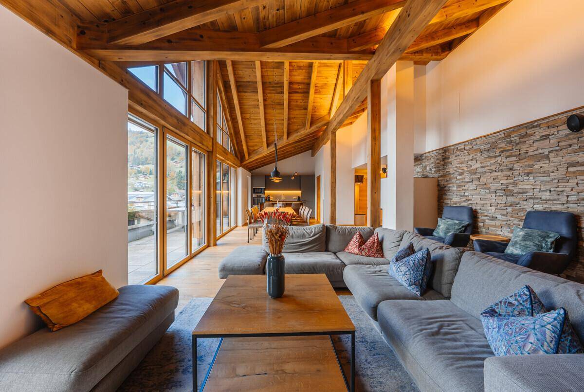 Gemütliches Wohnzimmer mit großem Sofa, Holzbalkendecke und Blick auf die Berge.