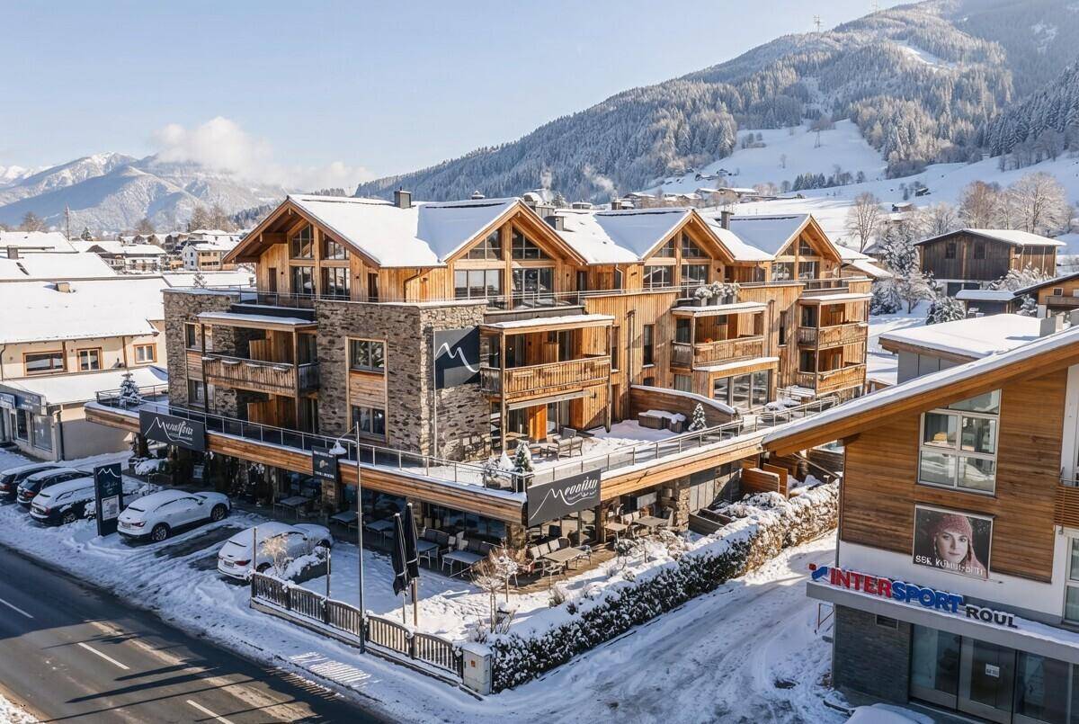 Luxuriöse Wohnanlage im alpinen Stil mit Stein- und Holzfassade in verschneiter Umgebung.