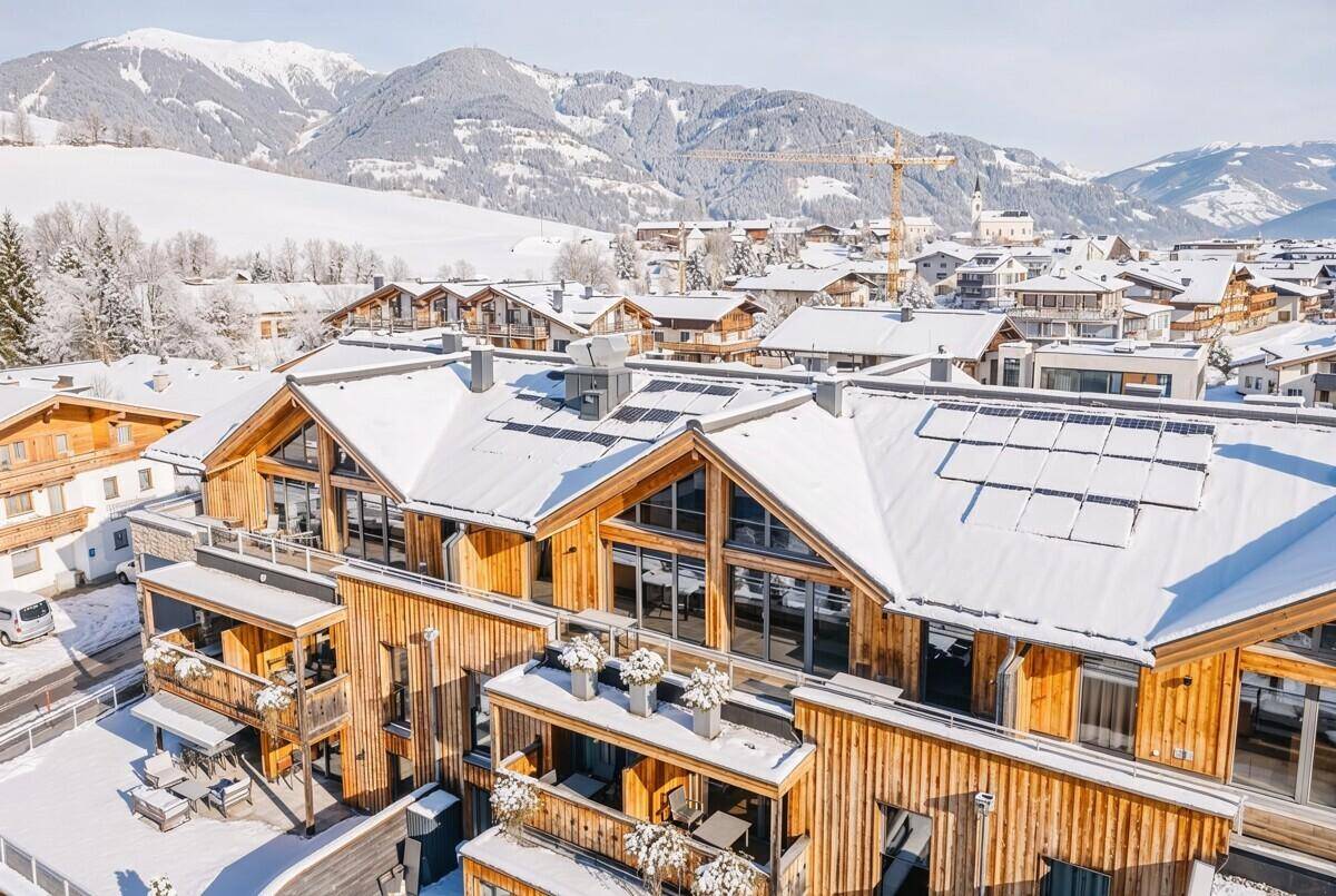 Neubau im alpinen Stil mit Holzfassade und Solarpaneelen, bedeckt mit Schnee.