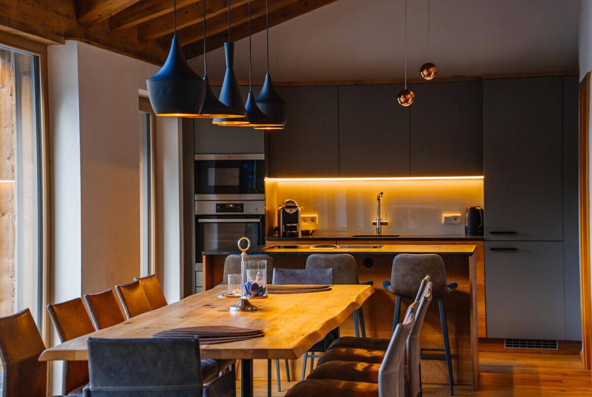 Moderne Küche mit dunklen Schränken, Holztisch und stilvoller Beleuchtung im Essbereich.