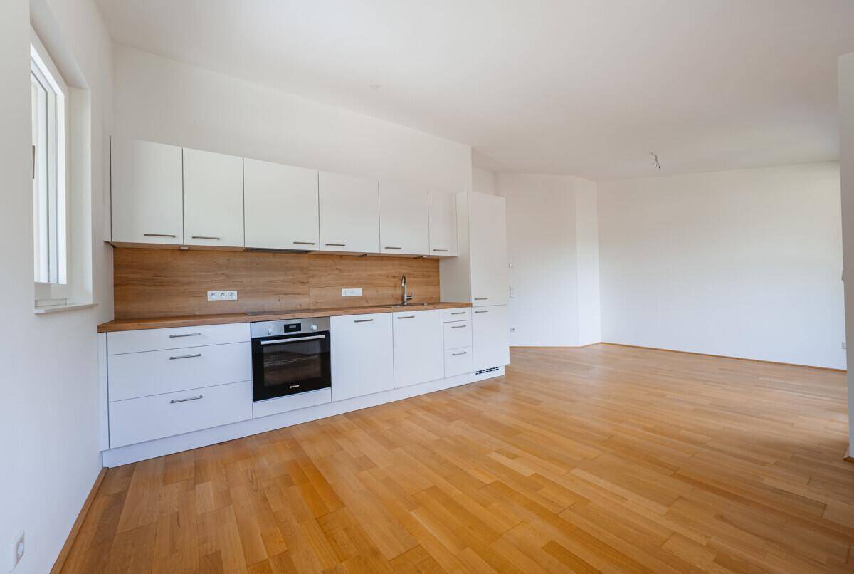 Moderne Einbauküche mit weißen Fronten, Holzarbeitsplatte und integriertem Backofen in einem hellen Raum.