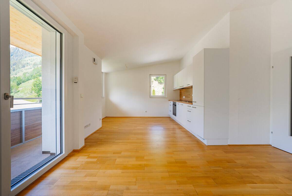 Geräumiger Wohnbereich mit Holzboden und großer Schiebetür, die Zugang zu einem Balkon mit Bergblick bietet.