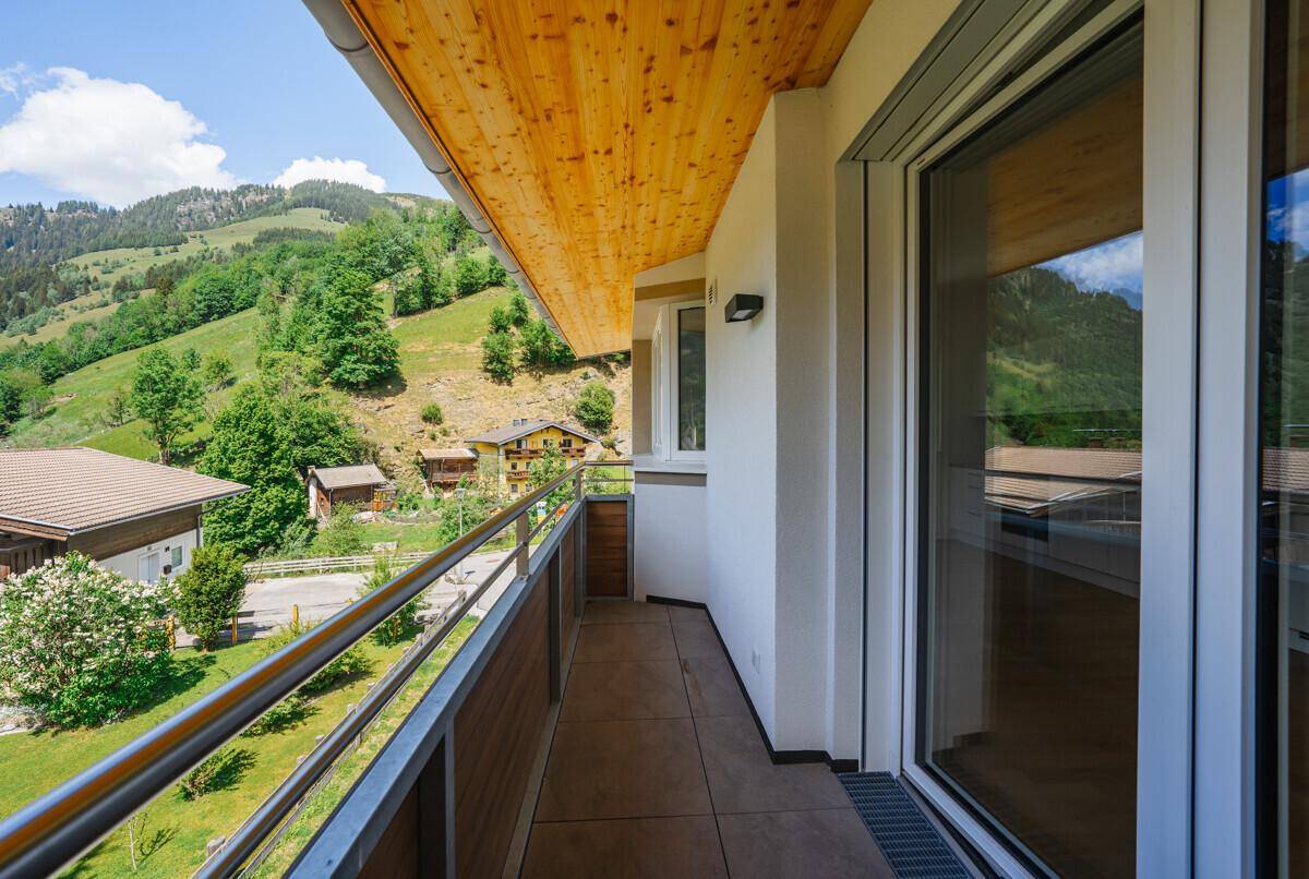 Geräumiger Balkon mit Holzdecke und Metallgeländer, der einen weiten Blick auf die grüne Berglandschaft bietet.