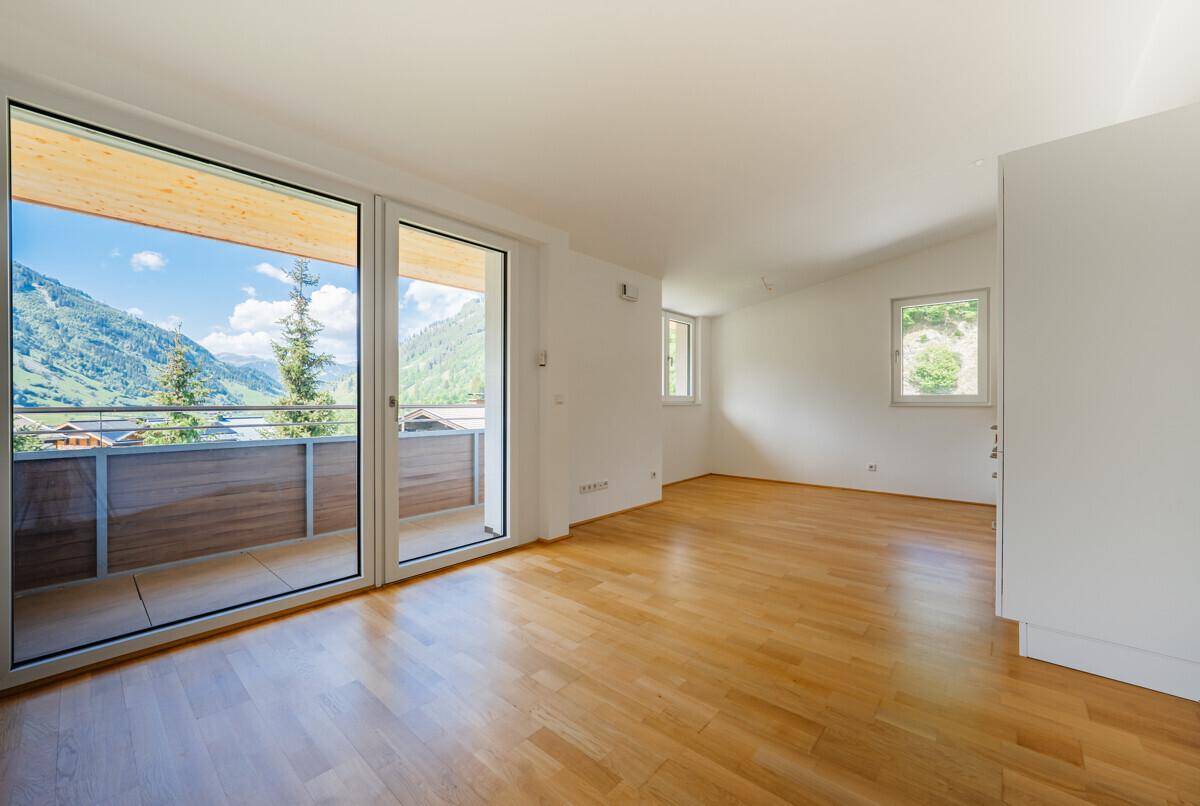 Lichtdurchfluteter Wohnbereich mit großen Fenstern und direktem Zugang zu einem Balkon mit beeindruckendem Bergblick.