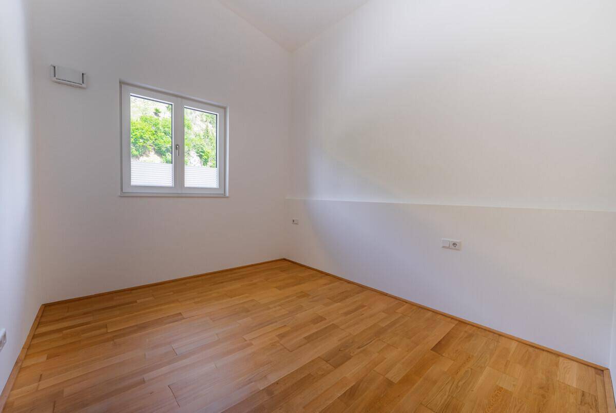 Helles Schlafzimmer mit Holzboden und einem Fenster, das viel Tageslicht in den Raum lässt.