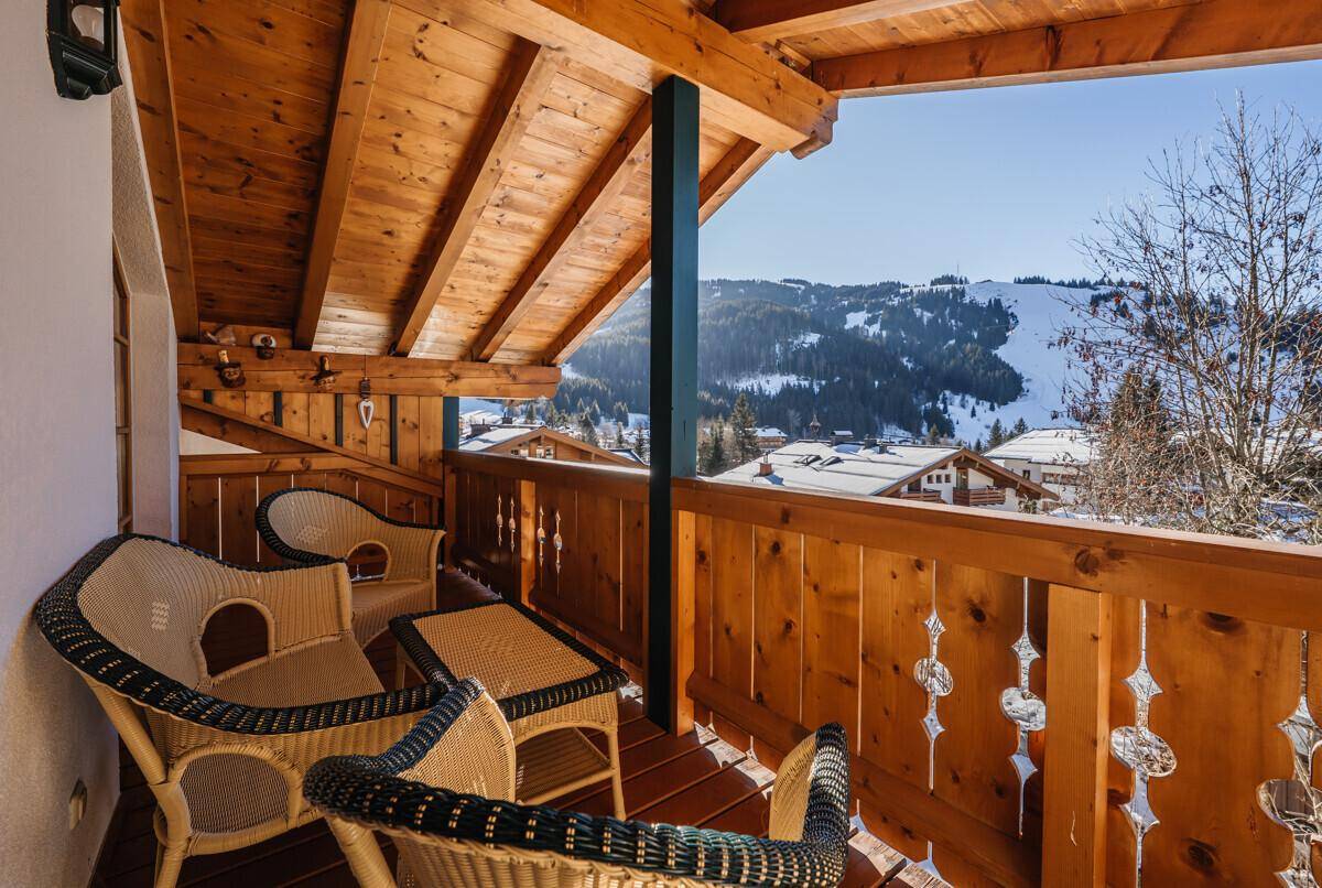 Überdachter Holzbalkon mit Sitzgelegenheiten und Panoramablick auf die verschneiten Berge.
