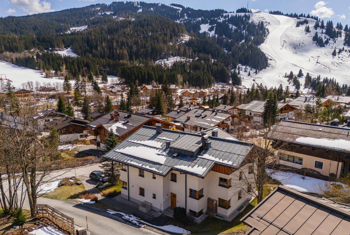 Luftaufnahme des Hauses in einer verschneiten Berglandschaft mit Skipisten im Hintergrund.