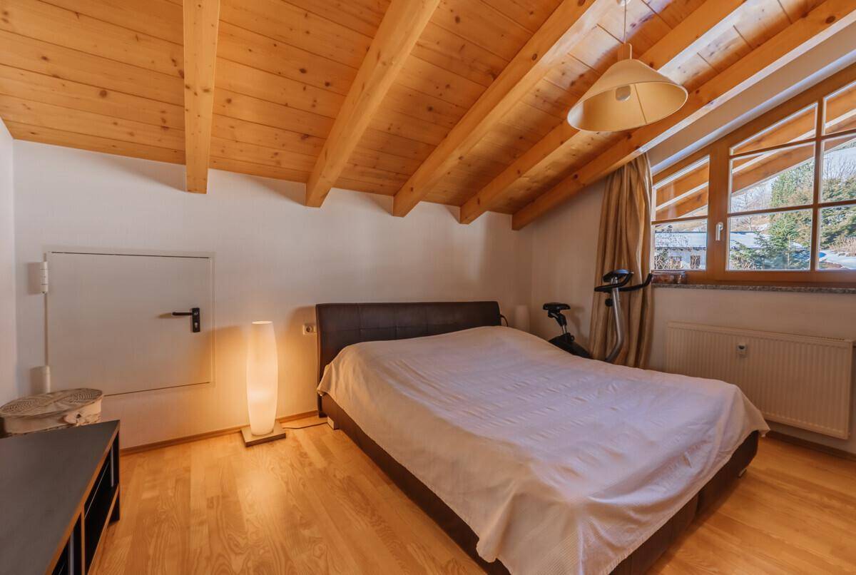 Schlafzimmer mit Holzbalkendecke, großem Fenster und Holzboden.