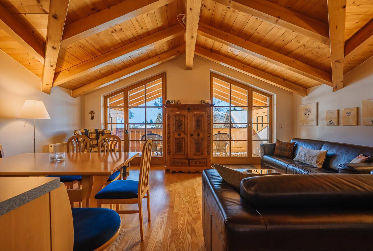 Gemütlicher Wohn- und Essbereich mit Holzbalkendecke, Ledersofas und Balkonzugang.