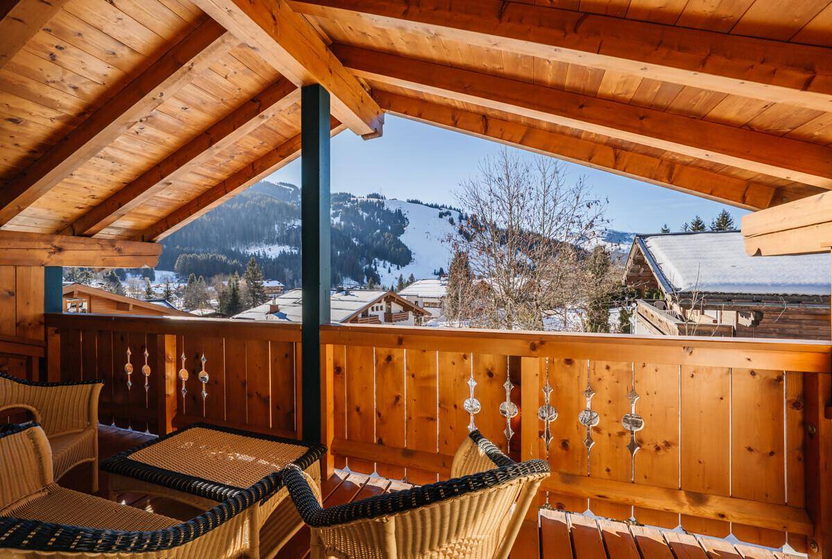 Geräumiger Holzbalkon mit weitem Blick auf die verschneite Berglandschaft und Sonnenschein.