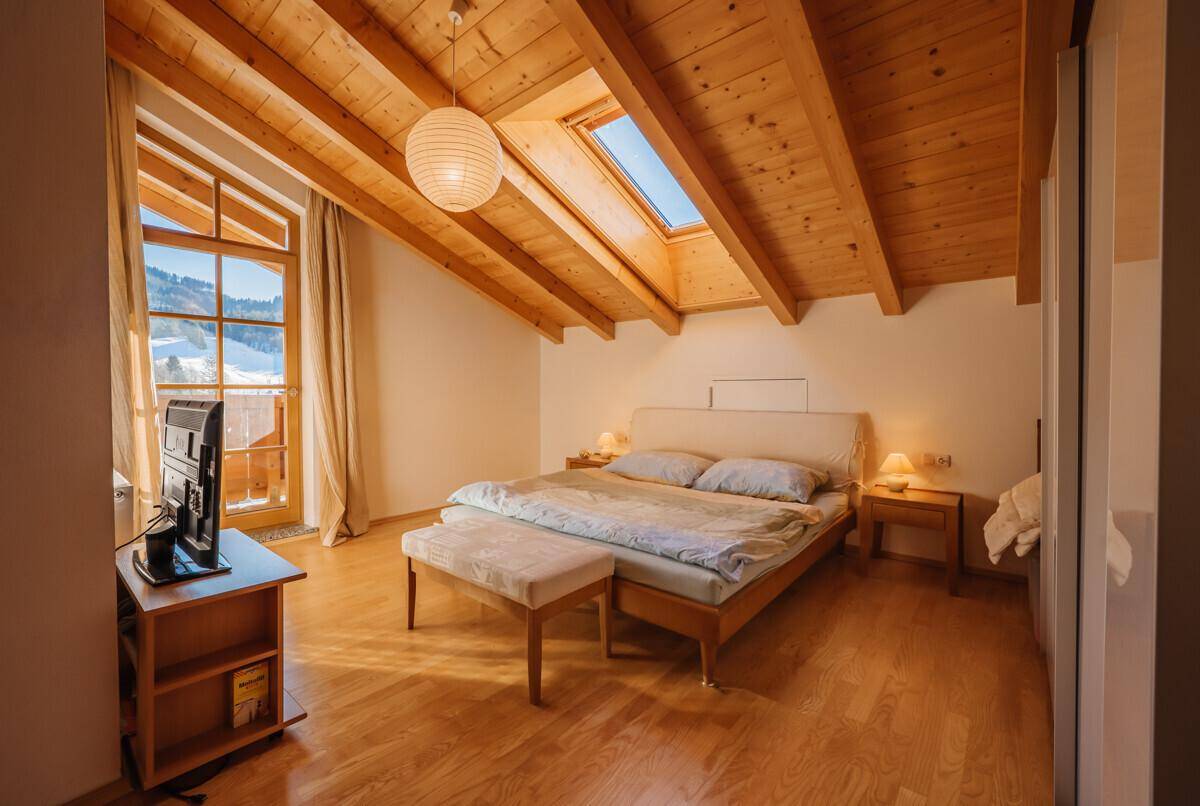 Helles Schlafzimmer mit Holzbalkendecke, Dachfenstern und Balkonzugang.
