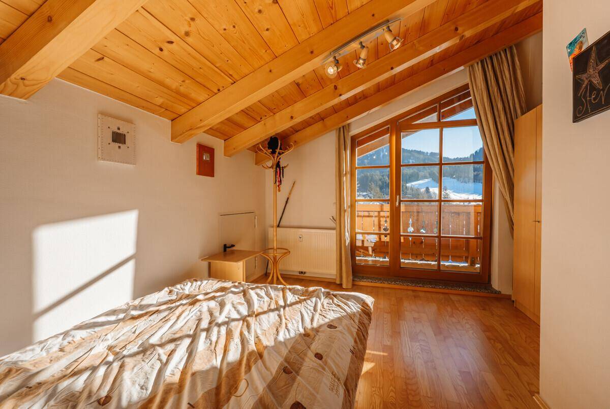 Gemütliches Schlafzimmer mit Holzbalkendecke und Zugang zu einem sonnigen Balkon.