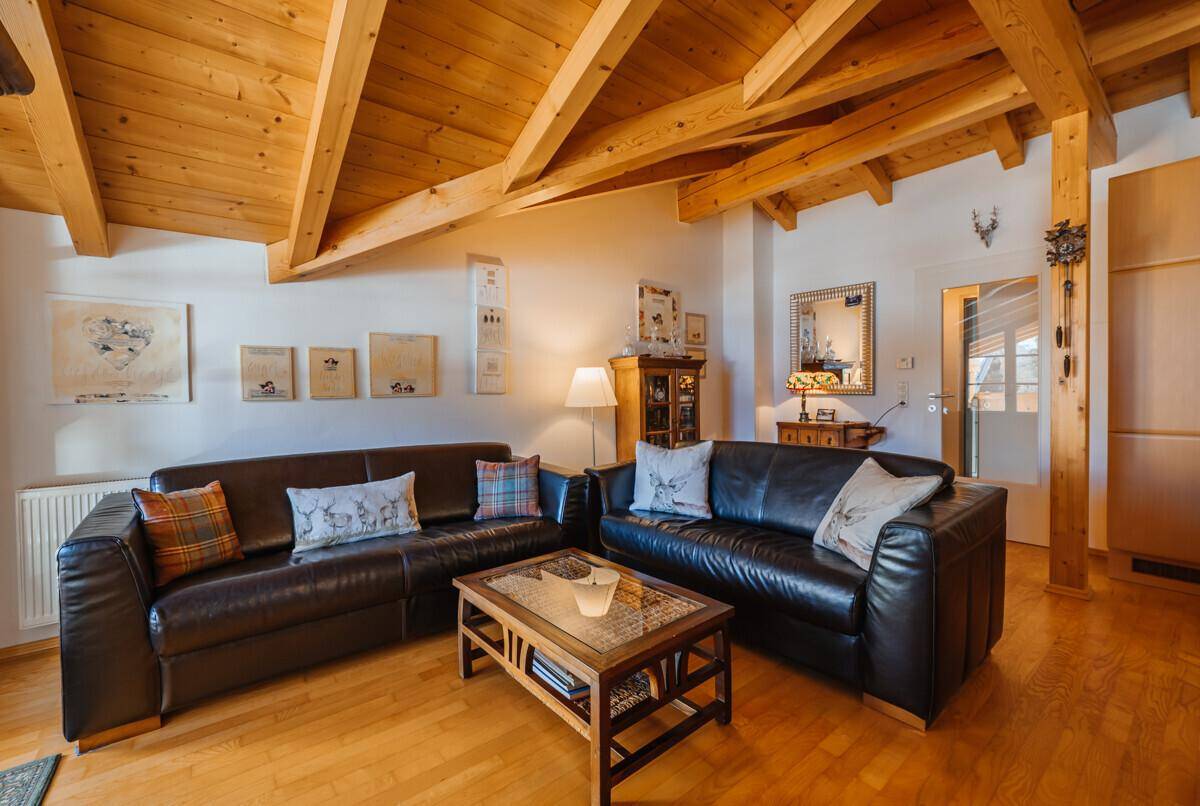 Wohnzimmer im alpinen Stil mit Holzbalkendecke, Ledersofas und traditioneller Dekoration.