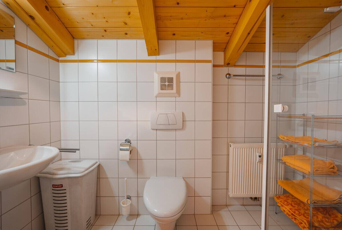 Badezimmer mit weißen Fliesen, Dusche und Holzbalkendecke.