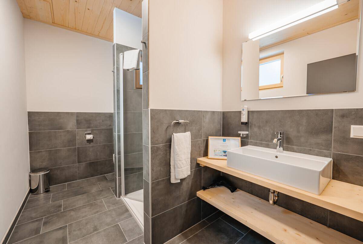 Modernes Badezimmer mit grauen Fliesen, ebenerdiger Dusche und Holzwaschtisch.
