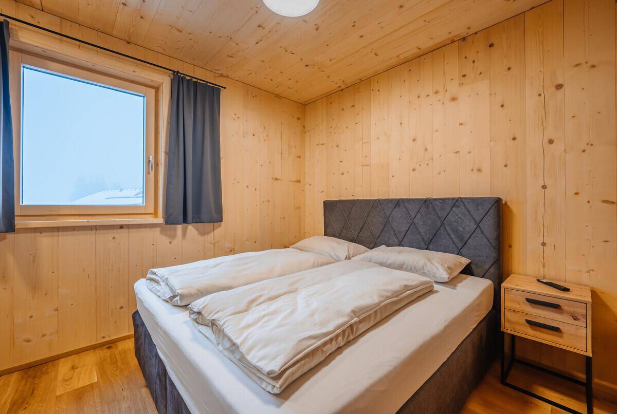 Helles Schlafzimmer mit Holztäfelung, komfortablem Bett und Fenster mit Blick nach draußen.
