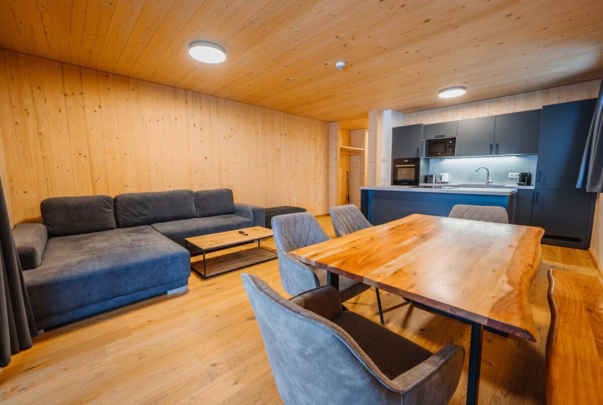 Heller Wohn- und Essbereich mit Holzwänden, bequemer Couch und großem Holztisch.