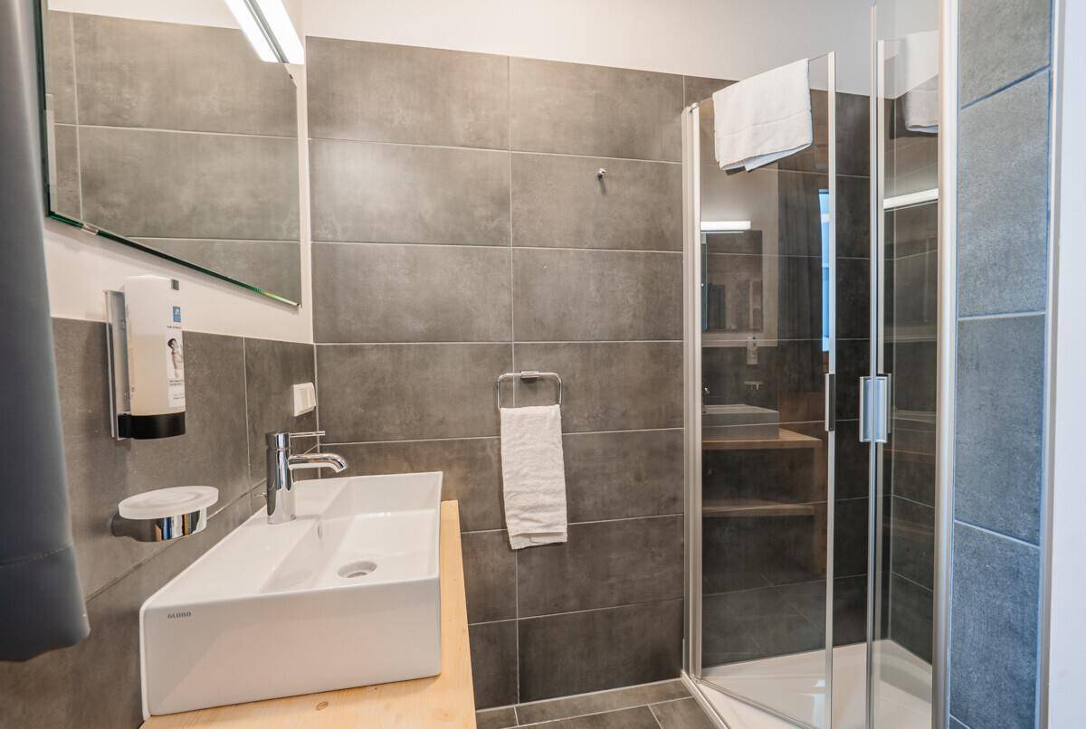 Modernes Badezimmer mit grauen Fliesen, stilvollem Waschbecken und Duschkabine.