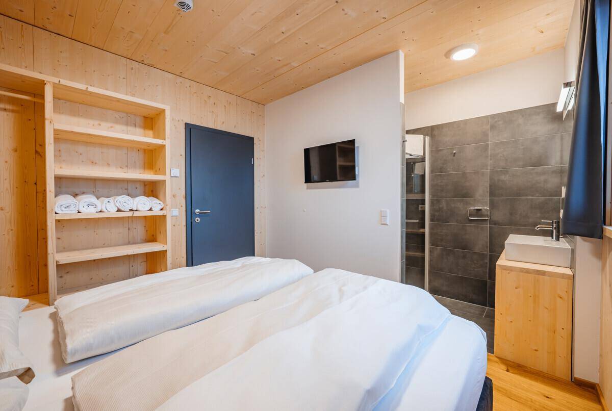 Schlafzimmer mit integriertem Badbereich, Holzelementen und praktischen Regalen.
