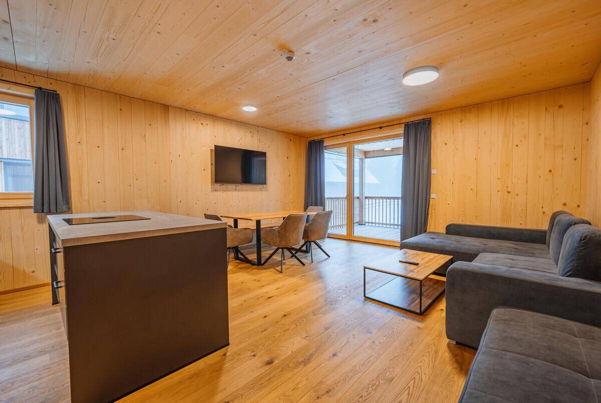 Heller Wohnbereich mit Holzboden, gemütlicher Sitzecke und Zugang zu einem Balkon mit Bergblick.