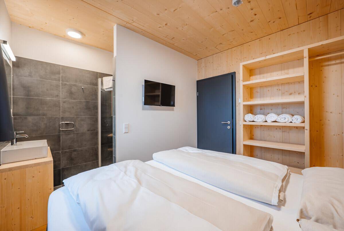 Gemütliches Schlafzimmer mit Holzwänden, offenem Kleiderschrank und integriertem Duschbereich.