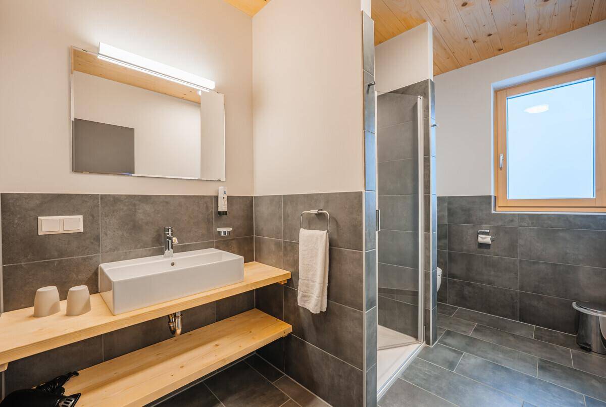 Modernes Badezimmer mit großformatigen grauen Fliesen, Holzablage und begehbarer Dusche.