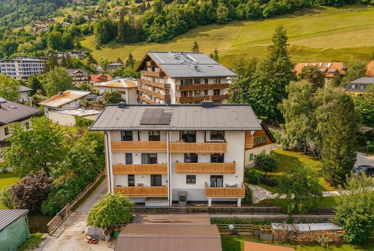 Luftaufnahme eines modernen Gebäudes mit Balkonen und Solaranlage auf dem Dach, umgeben von Natur.